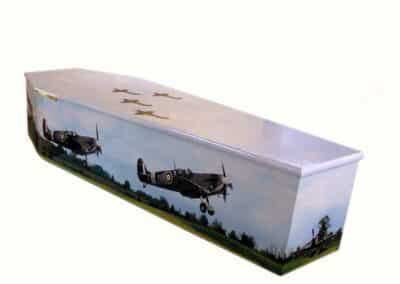 Bespoke coffin featuring Spitfire aircraft design with sky and landscape background